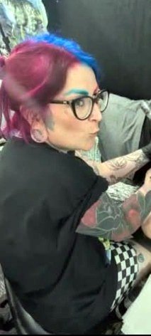 Grace Phillips tattooing at her station, pink and blue hair, focused on the work